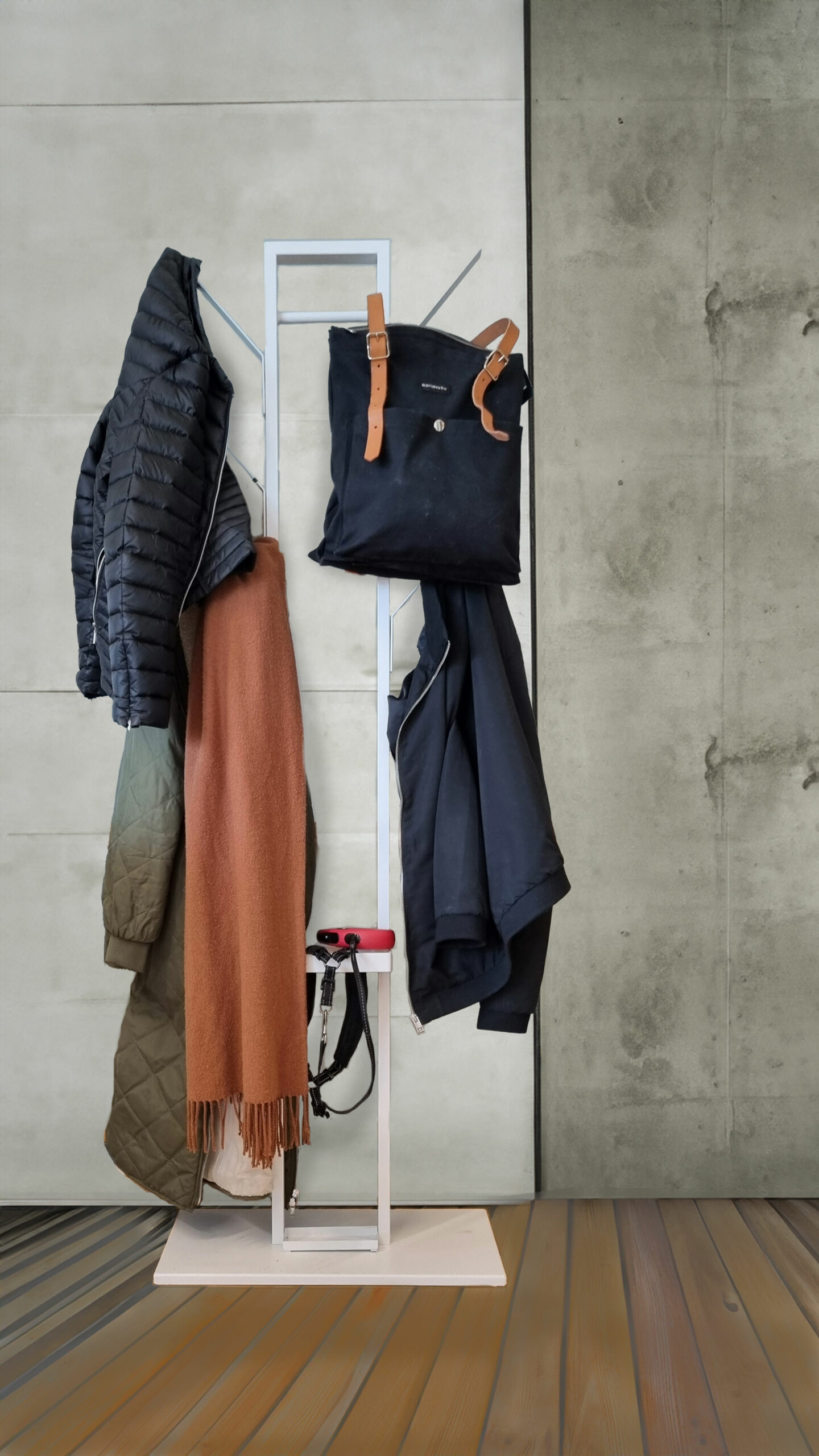 Valkoinen naulakko jossa roikkuu takkeja, reppu sekä kaulahuivi